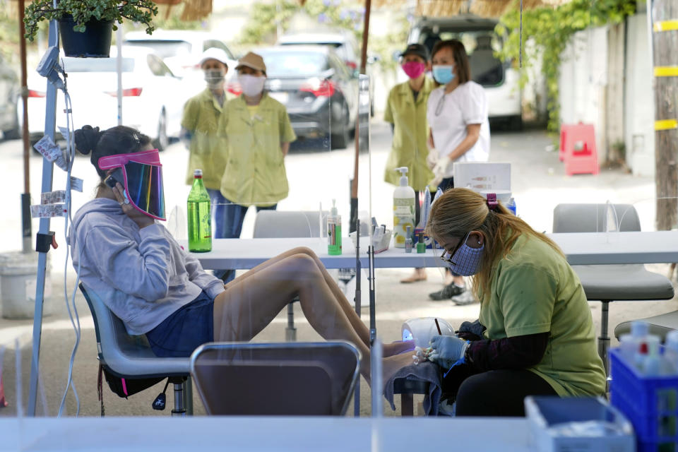 FILE - In this July 22, 2020, file photo, Tyson Salomon, left, gets a pedicure outside Pampered Hands nail salon in Los Angeles. A steady drop in coronavirus cases across California cleared the way Tuesday, Sept. 22, 2020, for the wider reopening of businesses in nine counties, including much of the San Francisco Bay Area, the state's top health official said. Dr. Mark Ghaly, the state health secretary, said nail salons could also reopen with restrictions, though he cautioned that California's reopening must remain "slow and stringent" and residents cannot let their guard down as flu season arrives and cases rise in Europe and other parts of the U.S. (AP Photo/Ashley Landis, File)