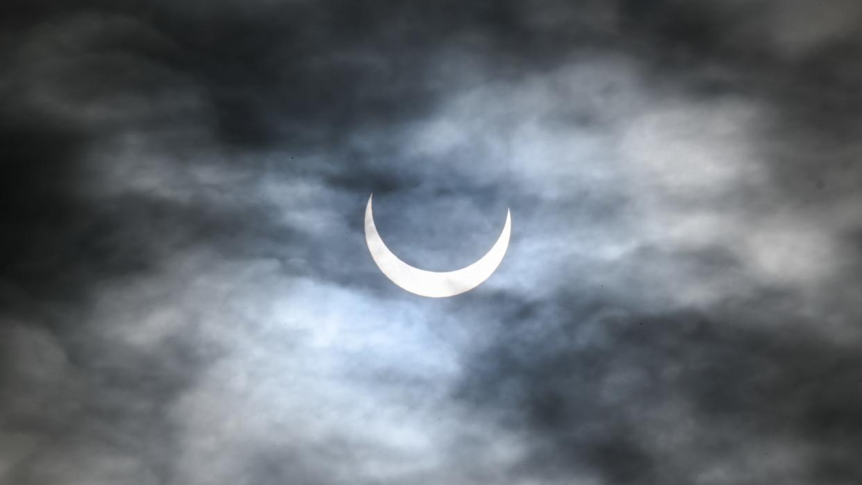  Behind wispy clouds, the moon can be seen partially blocking the sun. 