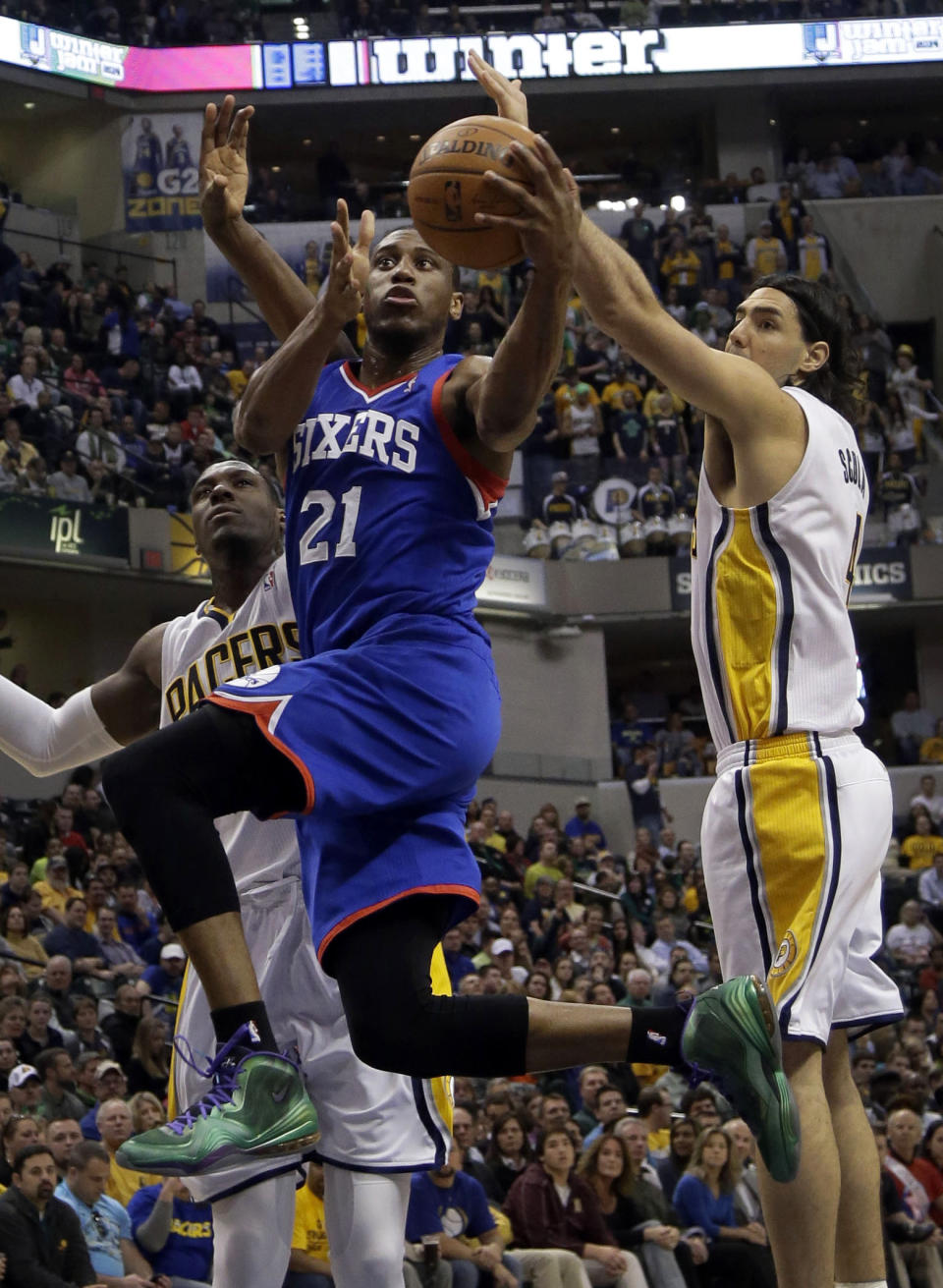 Philadelphia 76ers forward Thaddeus Young, center, drives between Indiana Pacers defenders Ian Mahinmi, left, and Luis Scola, of Argentina, during the first half of an NBA basketball game in Indianapolis, Monday, March 17, 2014. (AP Photo/AJ Mast)