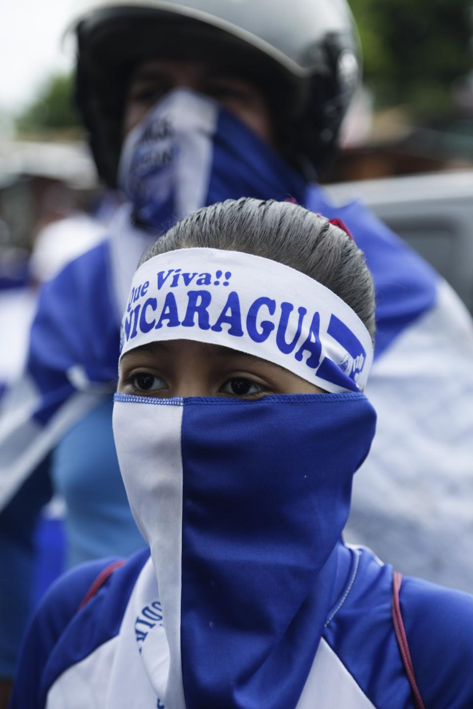 A girl covers her face with a bandana with colors of the Nicaraguan national flag during a protest outside the Jesuit run Universidad Centroamericana, UCA, demanding the university's allocation of its share of 6% of the national budget, in Managua, Nicaragua, Thursday, Aug. 2, 2018. Universities in Nicaragua are closed since mid-April as students are demanding the resignation of President Daniel Ortega and the release of all political prisoners. (AP Photo/Arnulfo Franco)