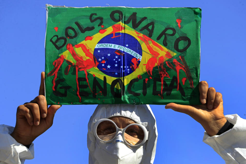 A demonstrator holds an image of the Brazilian flag covered in fake blood and the Portuguese phrase "Bolsonaro Genocide" during an anti-government protest by unions against President Jair Bolsonaro's policies to fight the COVID-19 pandemic in Brasilia, Brazil, Wednesday, May 26, 2021. (AP Photo/Eraldo Peres)