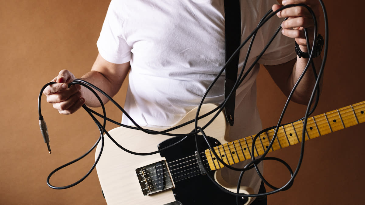  Man wearing a guitar holding a messy guitar cable in his hands. 