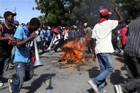 People circle a burning road block during protests in Port-au-Prince November 18, 2013. Thousands of Haitians took to the streets on Monday calling for President Michel Martelly to resign, and some protesters scuffled with police as international concern mounts over rising violence in the impoverished Caribbean nation. REUTERS/Stringer/Haiti