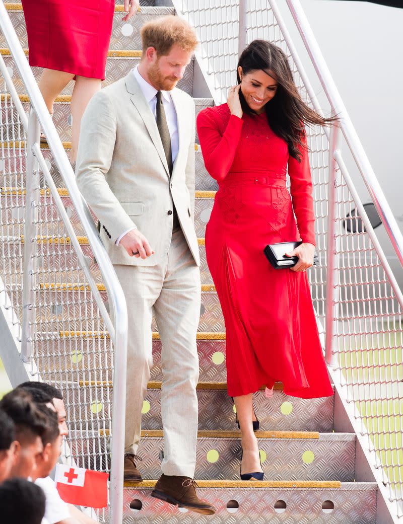<p> Meghan and Prince Harry arrived in Tonga as part of their 16-day royal tour. She wore a custom red Self-Portrait dress to honor the country&apos;s flag colors and re-wore her navy Manolo Blahnik heels and Dior clutch. </p>