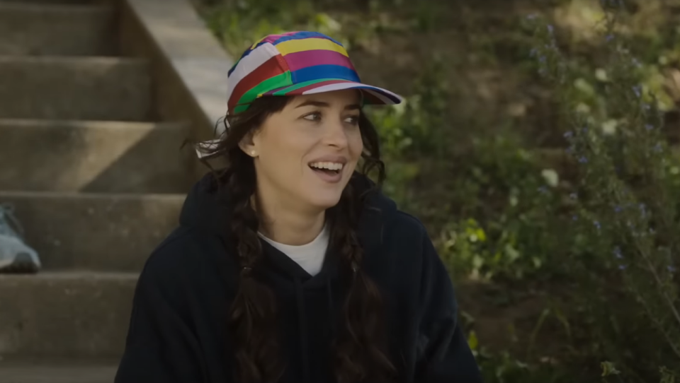 Dakota Johnson smiling in a rainbow hat in Am I OK?