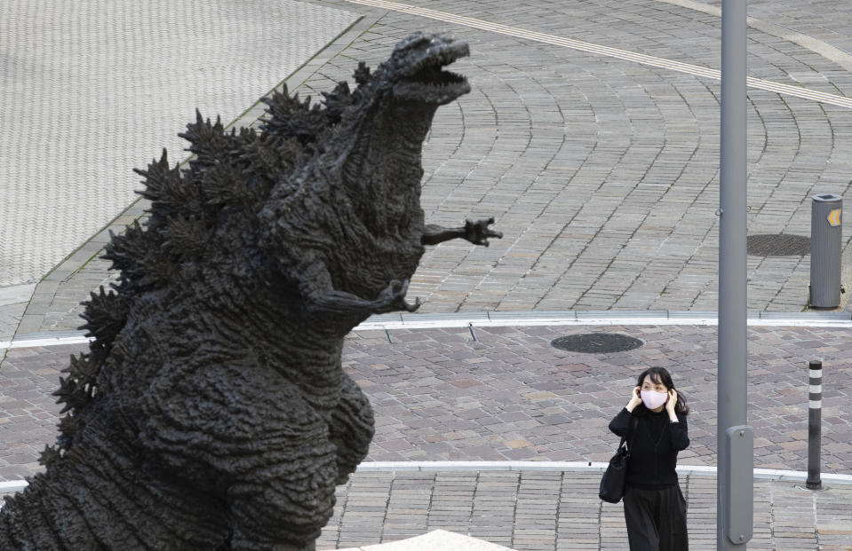 A woman adjusts her face mask as she walks by a statue of Godzilla in Tokyo Friday, Oct. 16, 2020. The Japanese capital confirmed more than 180 new coronavirus cases on Friday. (AP Photo/Hiro Komae)