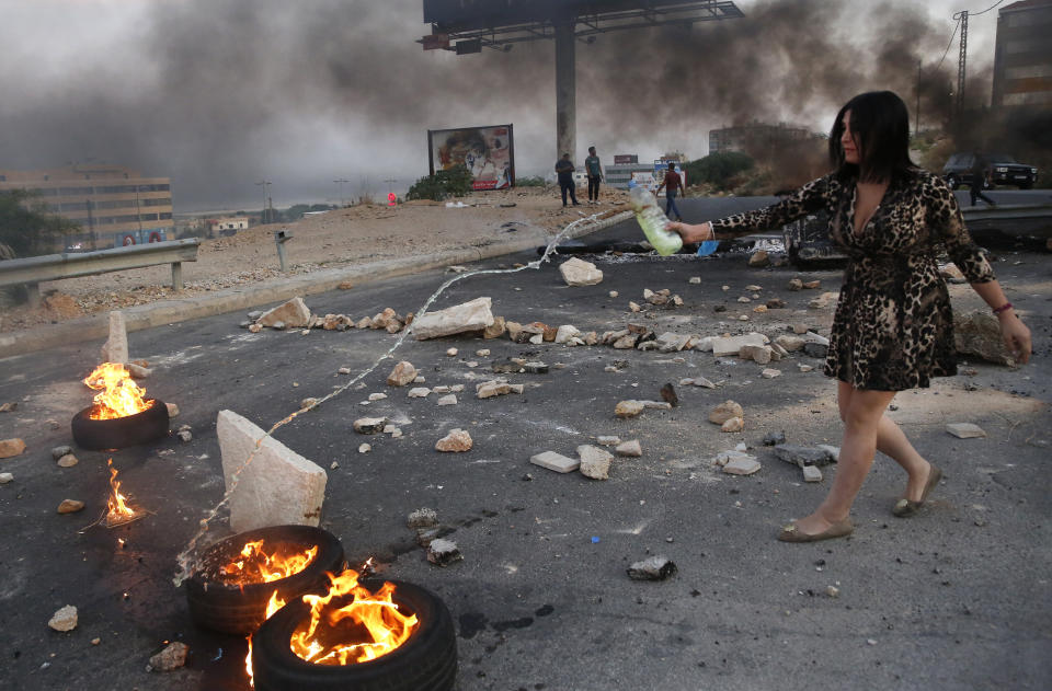 A protester throws oil over burn tires blocking the main highways during protests against corruption in Khaldeh, south of Beirut, Lebanon, Wednesday, Nov. 13, 2019. A local official for a political party was shot dead by soldiers trying to open a road closed by protesters in southern Beirut late Tuesday, the army reported, marking the first death in 27 days of nationwide protests. (AP Photo/Hussein Malla)