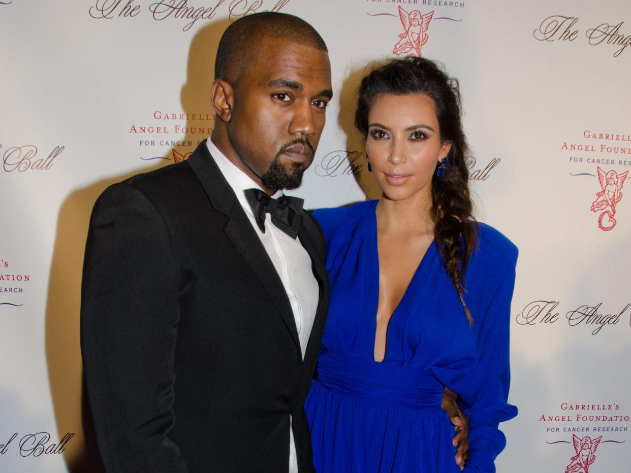 kim kardashian and ye on a red carpet. ye is wearing a tuxedo with a black bow tie, and kardashian is wearing a bright blue gown with a low-cut neckline and a slit up to her thigh