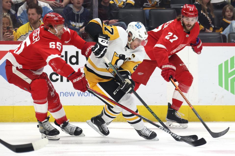 Sidney Crosby of the Pittsburgh Penguins battles for the puck between Danny DeKeyser (65) and Michael Rasmussen (27) of the Detroit Red Wings during the first period at Little Caesars Arena on April 23, 2022.