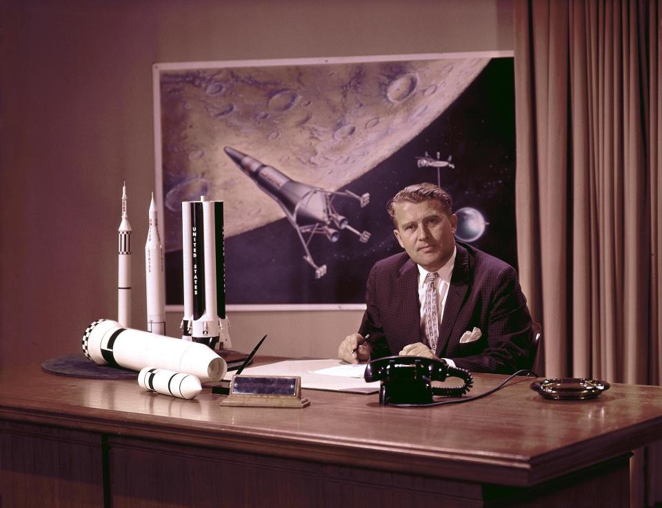 Wernher von Braun at his desk with moon lander in background and rocket models on his desk