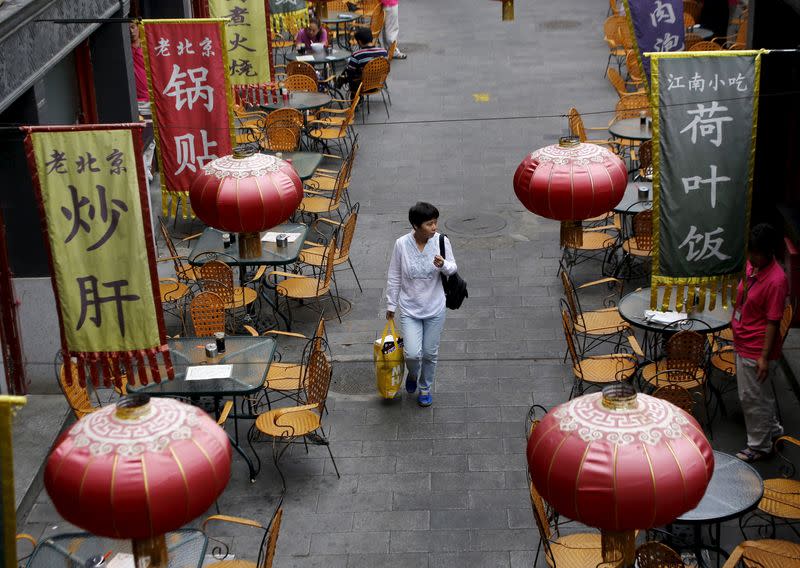 A woman carrying a shopping bag walks underneath lanterns of a restaurant in a shopping district of Beijing