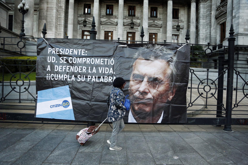 In this July 3, 2018 photo, a woman walks past an anti-abortion banner with a message that reads in Spanish: "Mr. President: You promised to defend life. Keep your word!", attached to the front gates of Congress. Macri has said he'd sign a measure that expands legal abortions if it passes, despite opposing abortion. (AP Photo/Jorge Saenz)