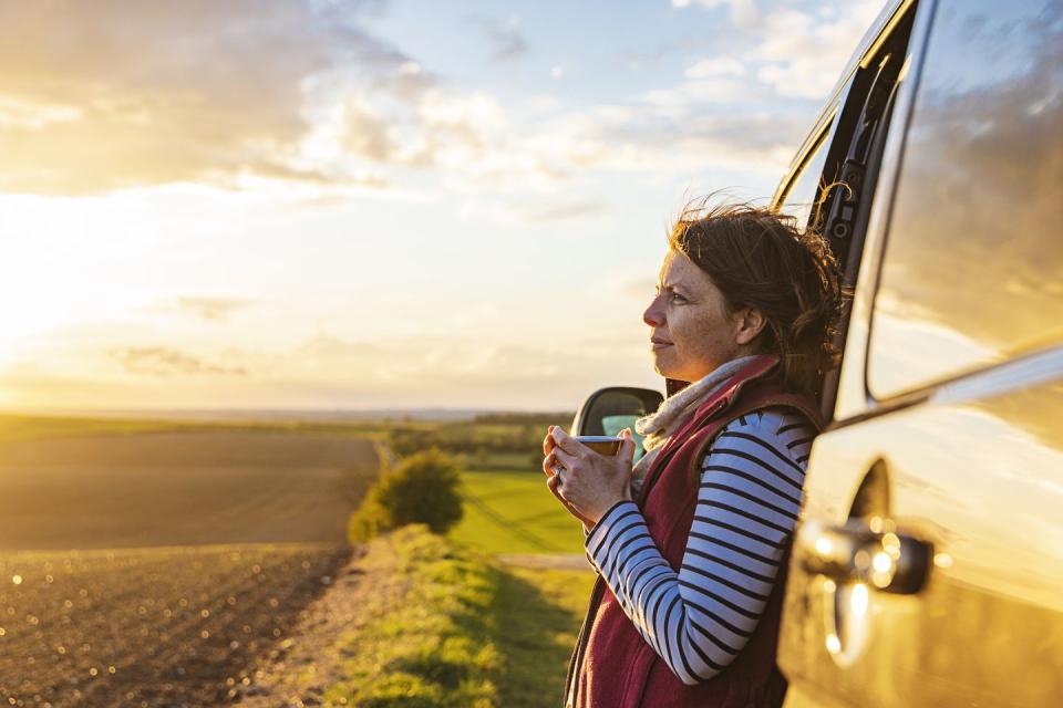 a woman in her 40s takes in the view of the countryside from her campervan she looks contented and relaxed