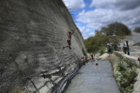 Un niño salta a una zanja que canaliza el agua de un túnel abandonado en Caracas, Venezuela, el 6 de junio de 2020. Hacía mucho que los obreros habían dejado de trabajar en un túnel de autopista que cruzaba la montaña. Sin embargo, el agua de manantial seguía acumulándose dentro del viaducto y discurría, malgastada, por delante de las casas. (AP Foto/Matías Delacroix)