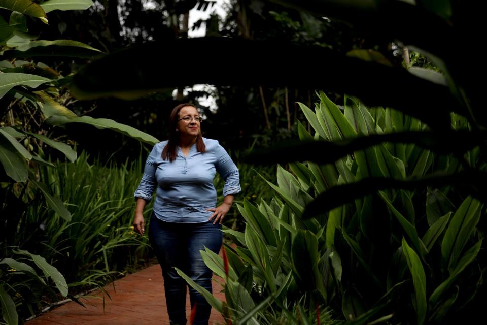 Woman stands with greenery around her.