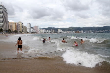 Tourists enjoy the waves as dark clouds brought by the proximity of tropical storm Carlos are seen in Acapulco, June 12, 2015. REUTERS/Claudio Vargas