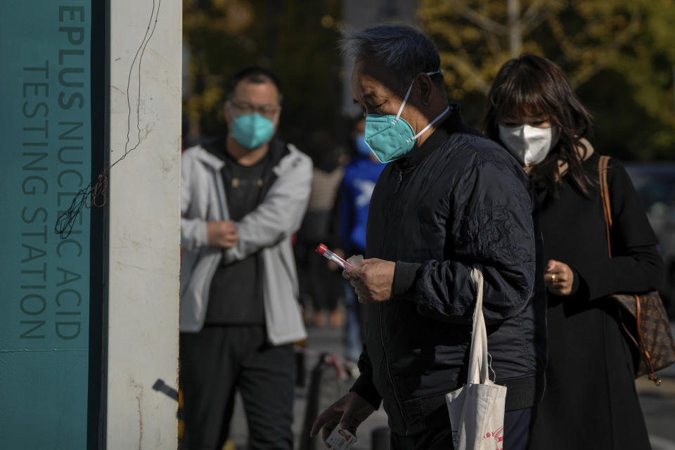 A man wearing a face mask holds his testing tube as masked residents line up for their routine COVID-19 throat swabs at a coronavirus testing site in Beijing, Monday, Oct. 31, 2022. (AP Photo/Andy Wong)