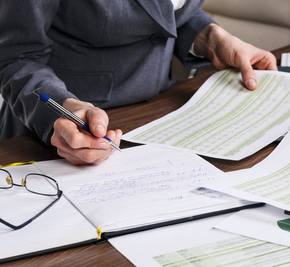 Close up of a female hand doing calculations on paper at an office desk.