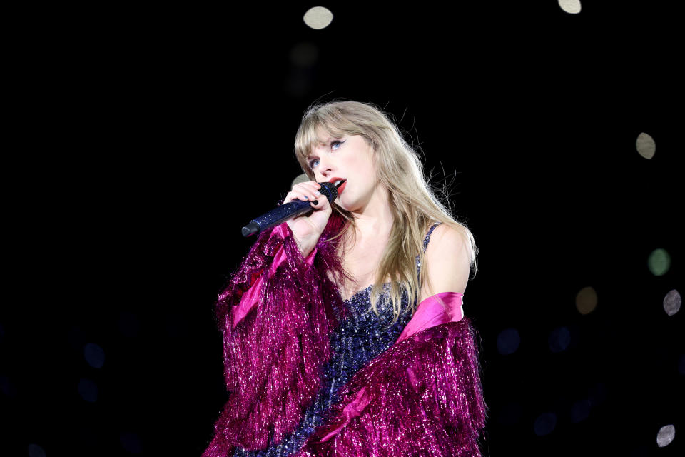 Taylor Swift on stage performing with a microphone, wearing a sparkly outfit