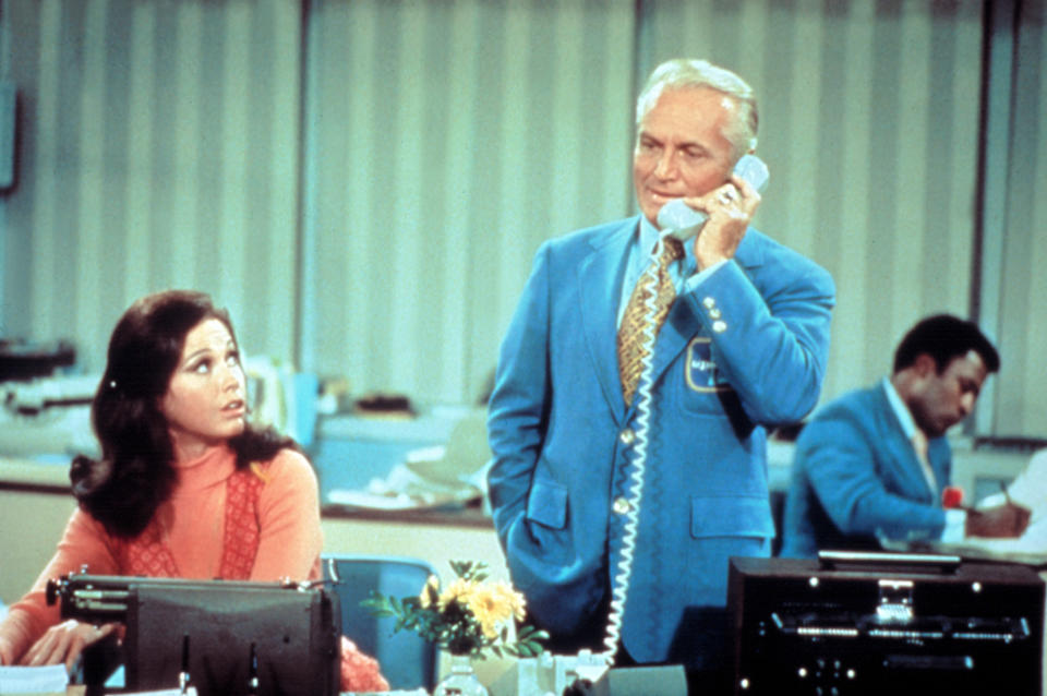 Mary Tyler Moore sits beside Ted Knight who is on the phone