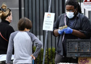 A social distancing sign is posted at the North Hollywood Farmer's Market as a produce vendor wearing a protective mask makes change for shoppers in Los Angeles on Saturday, April 4, 2020. The mayor of Los Angeles urged 4 million residents to wear masks to combat the coronavirus when they walk out in public. (AP Photo/Richard Vogel)