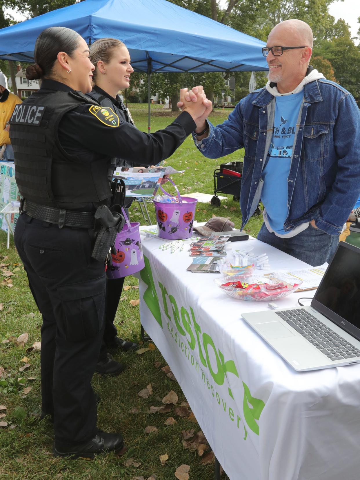 Cleveland Clinic Police Officers Leslie Alvarado, left, and Brie Schwab greet Restore Addiction Recovery resident Guy Nolan during a Faith & Blue event on Saturday, Oct. 7, 2023, in Akron, Ohio, at Hardest Park. [Phil Masturzo/ Beacon Journal]