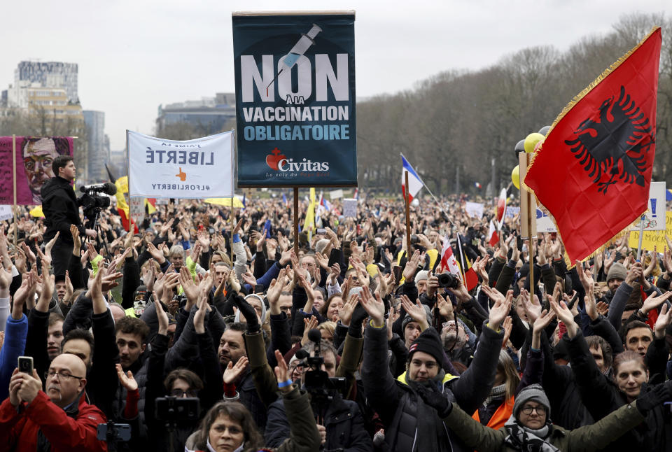 Protestors clap as they gather with signs and banners during a demonstration against COVID-19 measures in Brussels, Sunday, Jan. 23, 2022. Demonstrators gathered in the Belgian capital to protest what they regard as overly extreme measures by the government to fight the COVID-19 pandemic, including a vaccine pass regulating access to certain places and activities and possible compulsory vaccines. Banner at center reads 'No to obligatory vaccines'. (AP Photo/Olivier Matthys)