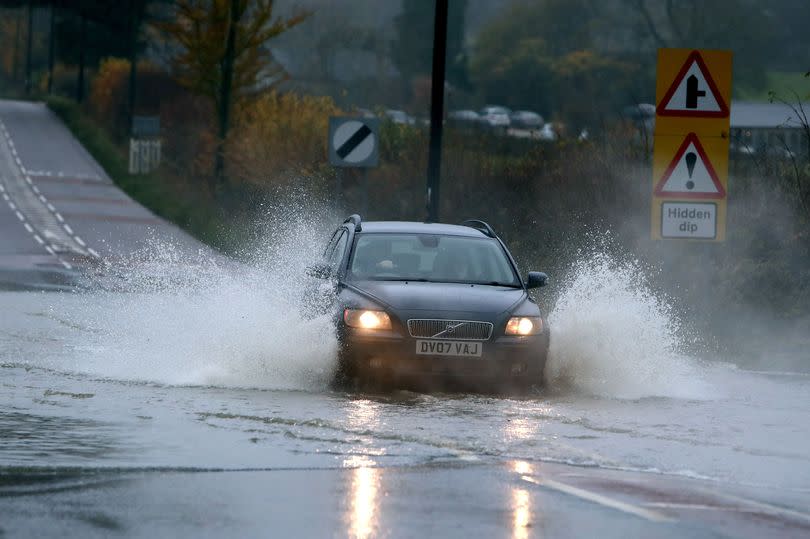 A car goes through flood water on a road outside Atworth, Wiltshire