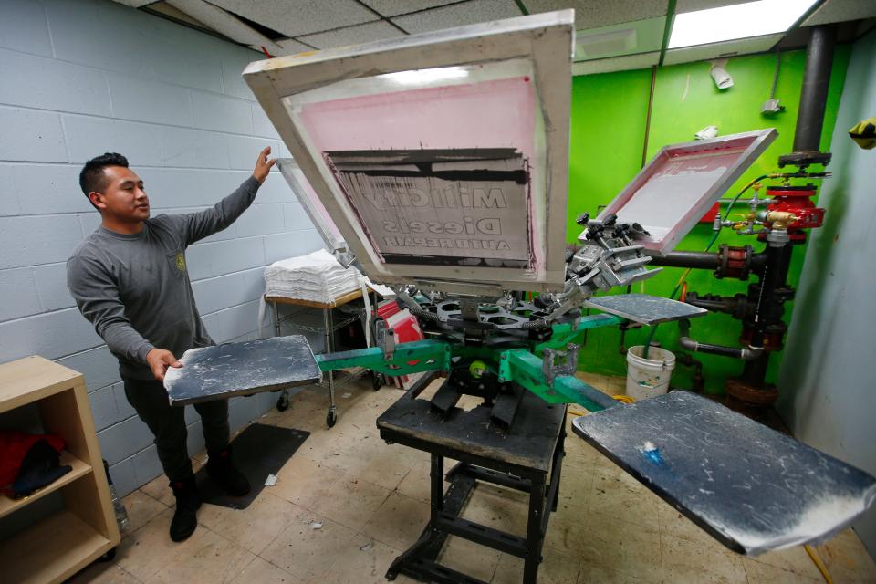 Carlos Chamorro, co-owner, rotates the screen printing machine at the recently opened Ocean Drive Screenprinting on MacArthur Drive in New Bedford.