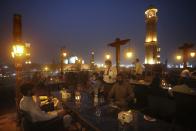 People eat at a rooftop restaurant close to the historical Badshahi Mosque, following an ease in restrictions that had been imposed to help control the coronavirus, in Lahore, Pakistan, Tuesday, Aug. 11, 2020. Pakistan's daily virus infection rate has stayed under 1,000 for more than four weeks prompting the government to further ease restrictions for restaurants, parks, gyms and cinemas. (AP Photo/K.M. Chaudary)