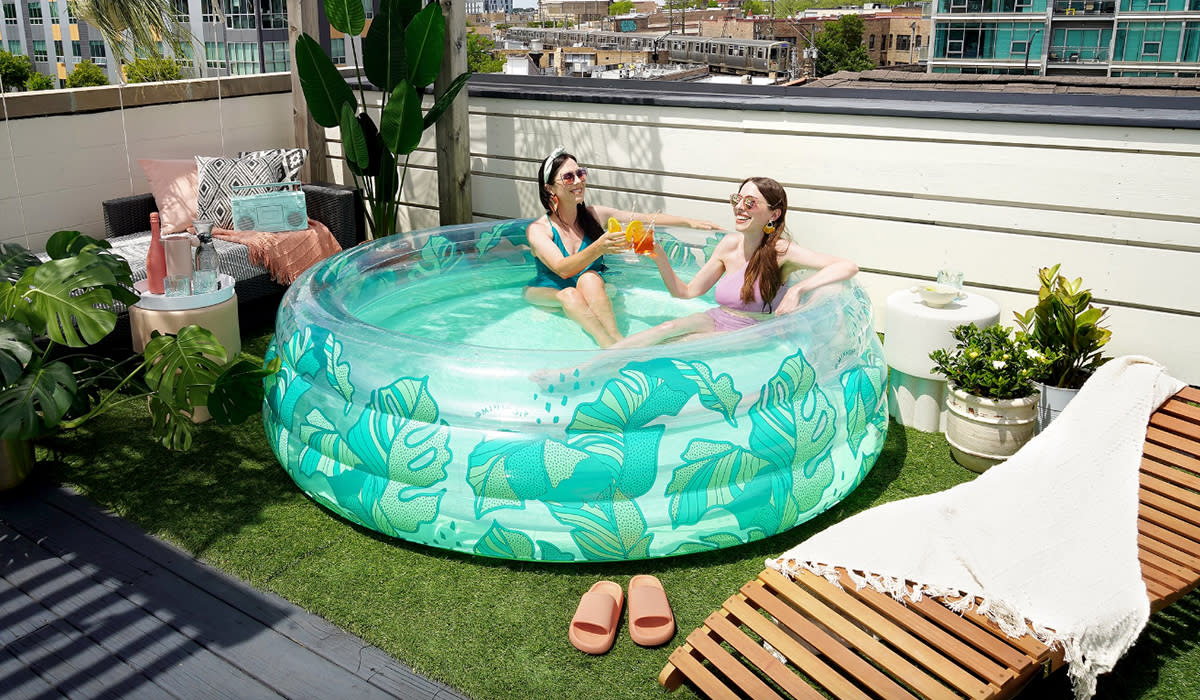 Two grown women cheersing with beverages in inflatable pool on rooftop