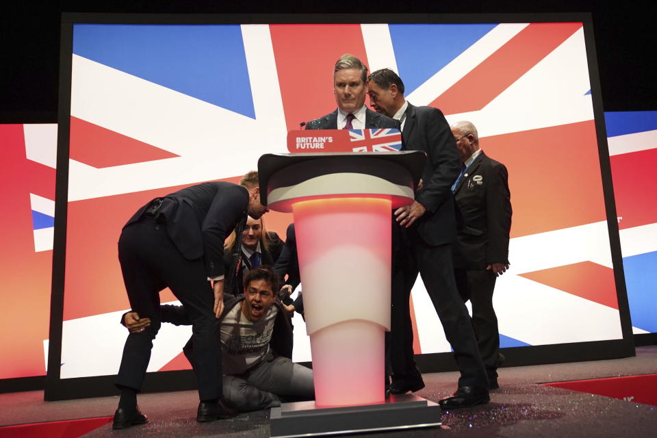 A protester is dragged away after throwing glitter and disrupting Labour leader Sir Keir Starmer making his keynote speech during the Labour Party conference in Liverpool, England, Tuesday, Oct. 10, 2023. (Stefan Rousseau/PA via AP)