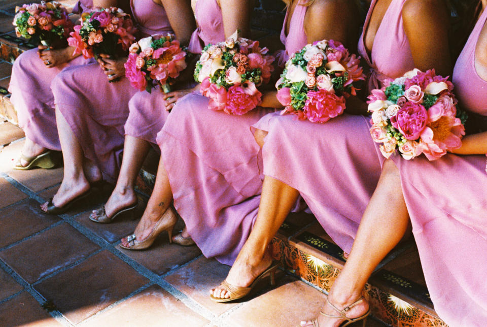 bridesmaids in pink dresses with bouquets sitting on the stairs