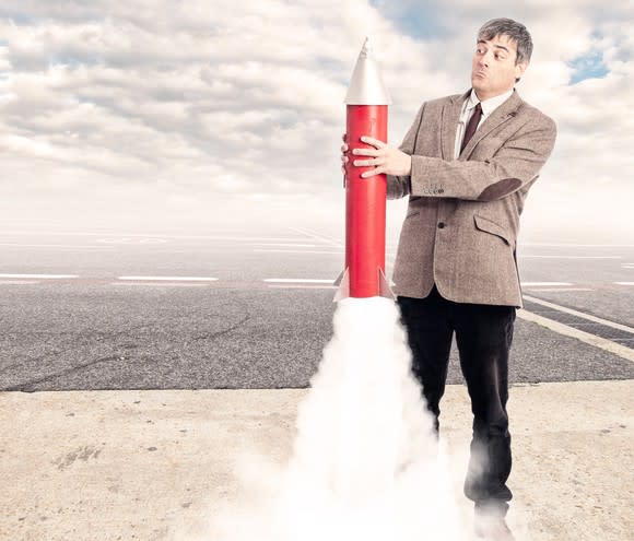 A man with a surprised look holds a toy rocket that's starting to launch.