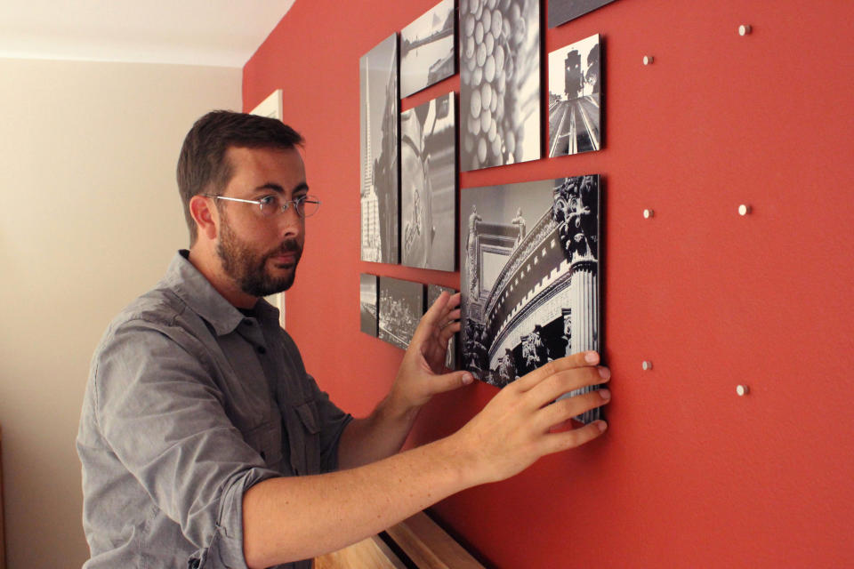 In this undated publicity photo provided by CollageWall Inc., Jason Rodman installs a collagewall display that he designed and photographed in a a bedroom in San Francisco. Previsualize your wall online, then order the paper grid template, push pegs and photos from Collagewall.com. Family, vacation and personal interest pictures are some of the themes you can use to create a photographic salon wall. (AP Photo/CollageWall Inc., Jason Rodman)