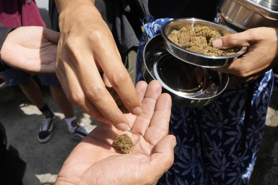 A cannabis supporter give a free piece of cannabis to fellow supporters at a demonstration outside the Government House in Bangkok, Thailand, Tuesday, Nov. 22, 2022. Thailand made it legal to cultivate and possess marijuana for medicinal purposes earlier this year, but lax regulations allowed the growth of a recreational marijuana industry, and the demonstrators don't want the rules against it to be strengthened again. (AP Photo/Sakchai Lalit)