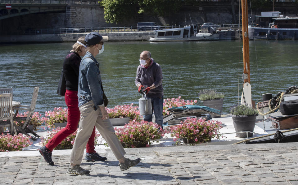 People wear masks to help curb the spread of the coronavirus walk past a man who watering flower on his boat at the Seine river in Paris, Monday, May 18, 2020 as France gradually lifts its Covid-19 lockdown. (AP Photo/Michel Euler)