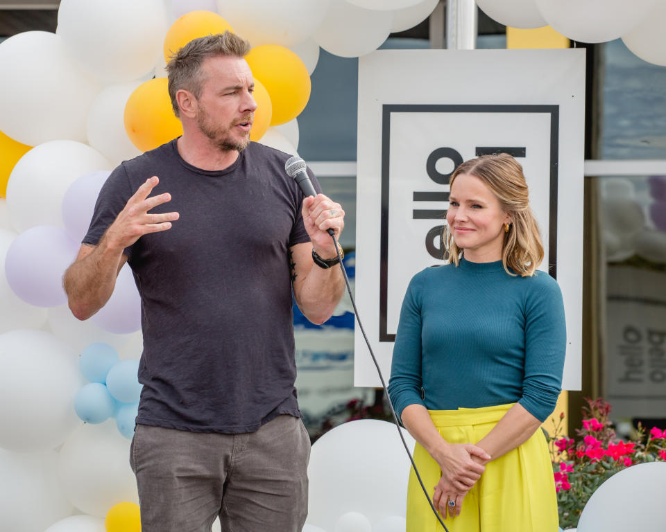 Dax speaking into a microphone as Kristen looks on