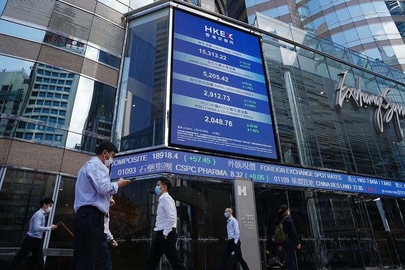 FILE PHOTO: People walk past a screen displaying the Hang Seng stock index at Central district, in Hong Kong