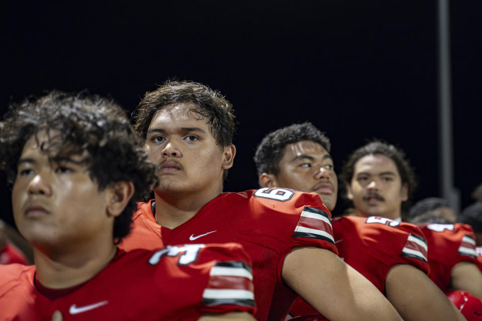 Lahainaluna High School football offensive lineman (63) Morgan "Bula" Montgomery, second from the left, lines up before singing the national anthem Saturday, Oct. 21, 2023, in Lahaina, Hawaii. Lahainaluna’s varsity and junior varsity football teams are getting back to normal since the devastating wildfire in August. (AP Photo/Mengshin Lin)