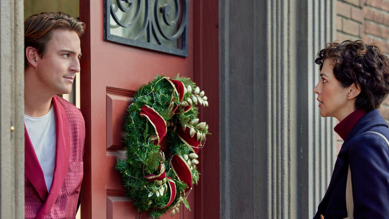  Evan Roderick, Katie Findlay talk in a doorway with a wreath in Sealed with a List. 