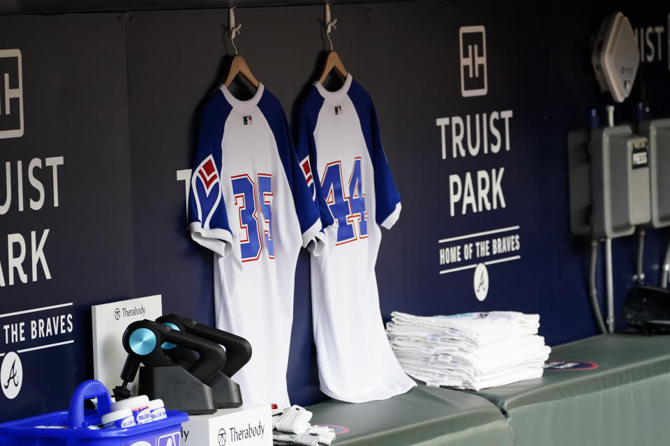 Atlanta Braves jerseys baring the numbers (35) for former Braves players Phil Niekro and (44) for Hank Aaron are hung in the dugout before a baseball game against the Philadelphia Phillies, Friday, April 9, 2021, in Atlanta. Both Aaron and Niekro died in the off season. (AP Photo/John Bazemore)