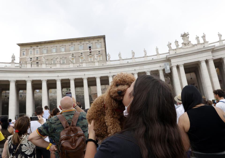 A girl kisses her dog as Pope Francis, background top, celebrates the Angelus prayer from his studio window overlooking St. Peter's Square at the Vatican, Sunday, July 25, 2021. Pope Francis has offered his blessing for the Tokyo Olympic Games from Vatican City. Francis told the faithful gathered in St. Peter’s Square for the traditional papal blessing that “in this period of pandemic, these Games are a sign of hope, a sign of universal brotherhood and of a healthy competitive spirit.” (AP Photo/Riccardo De Luca)