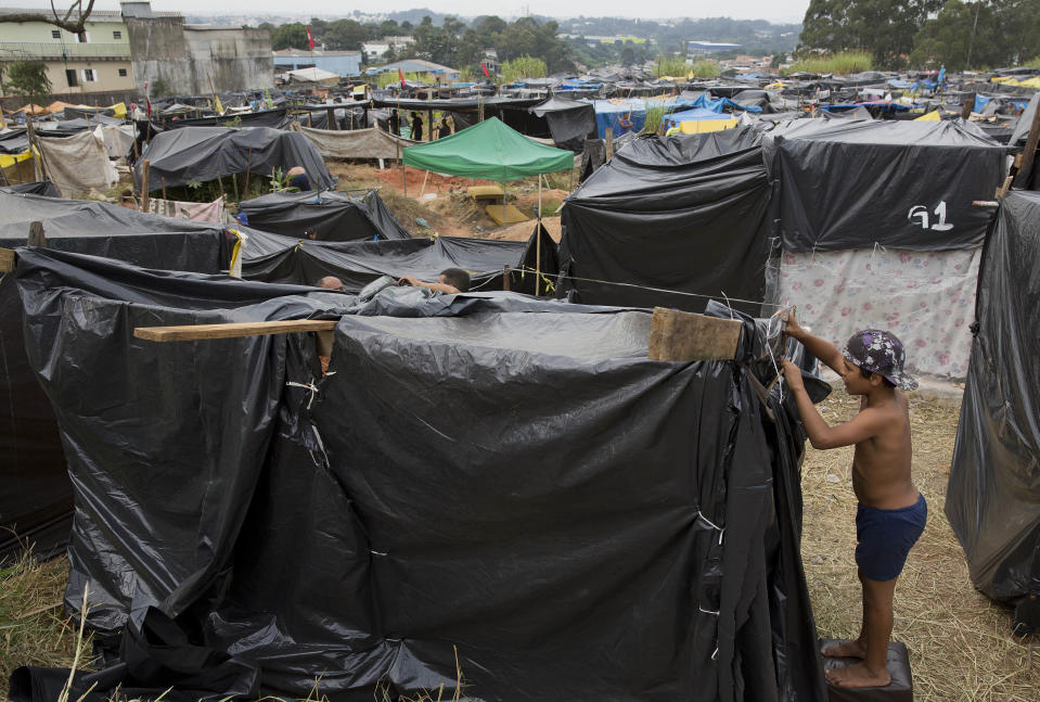 A boy helps his father build a shack on occupied land within view of the Itaquerao stadium, which will host the World Cup opener, in Sao Paulo, Brazil, Tuesday, May 6, 2014. The residents of the new tent village two miles away from the stadium say the neighborhood’s rent went up as a result of the World Cup real-estate fever in their neighborhood, driving them out of their homes. (AP Photo/Andre Penner)