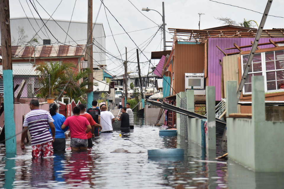 People walk in a flooded street next to damaged houses in Puerto Rico on Sept. 21, 2017, after Hurricane Maria hit. (Photo: AFP Contributor via Getty Images)