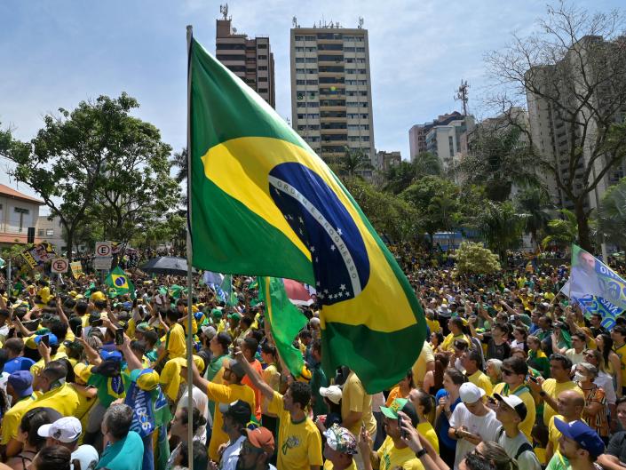 Сторонники президента Бразилии Жаира Болсонару размахивают бразильским флагом во время предвыборного митинга.