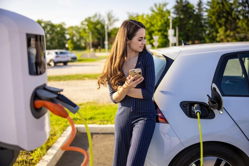 A person checks a smartphone while charging an electric vehicle.