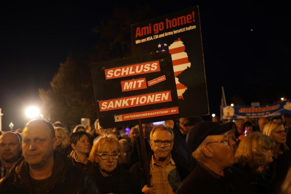 A man holds a sign that reads: “Ami Go Home! How the NSA, CIA and Army hold us occupied,” while another holds a sign that reads: “Enough with Sanctions” during a Monday night protest in October in Schwerin.