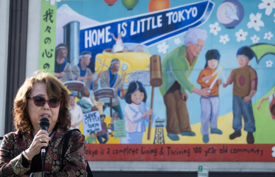 A woman holds a microphone in front of a colorful mural of people.