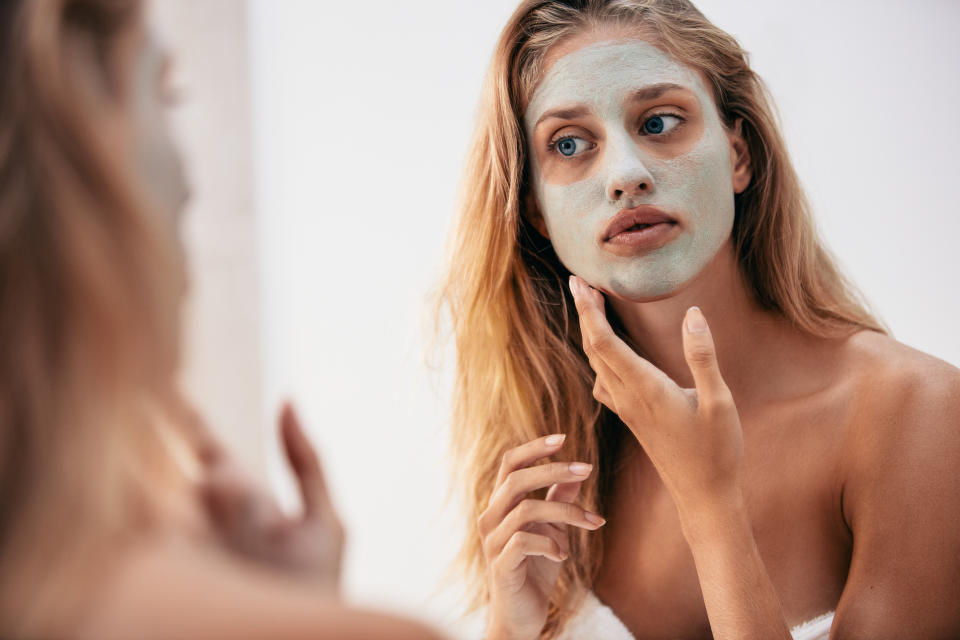 Woman looking in the mirror with mask on her face. Female applying facial cosmetic mask in bathroom.